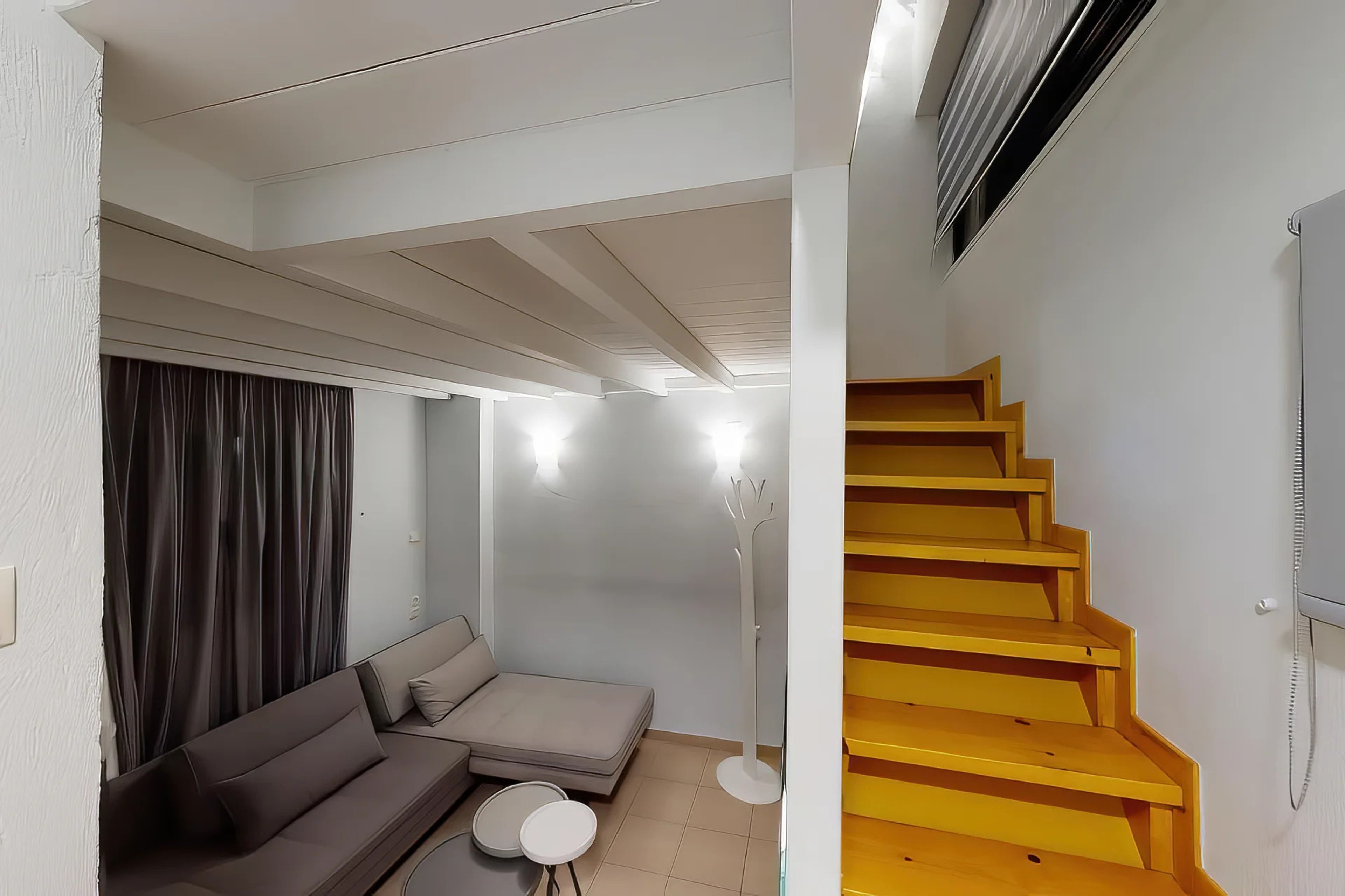 Ein Wohnzimmer mit einer Couch, einem kleinen Tisch, einer Stehlampe und einer Treppe mit Holzstufen.