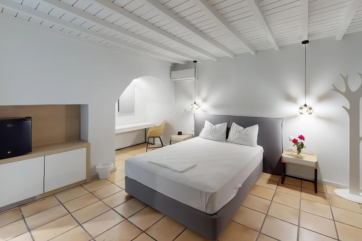 Un dormitorio moderno con cama, mesitas de noche, un televisor y una original decoración en forma de árbol en la pared.