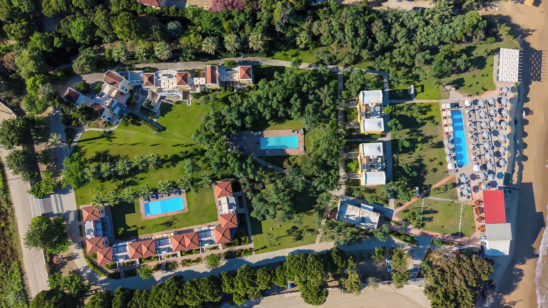 Vista aérea de un resort con varias edificaciones, una piscina y una zona de playa.