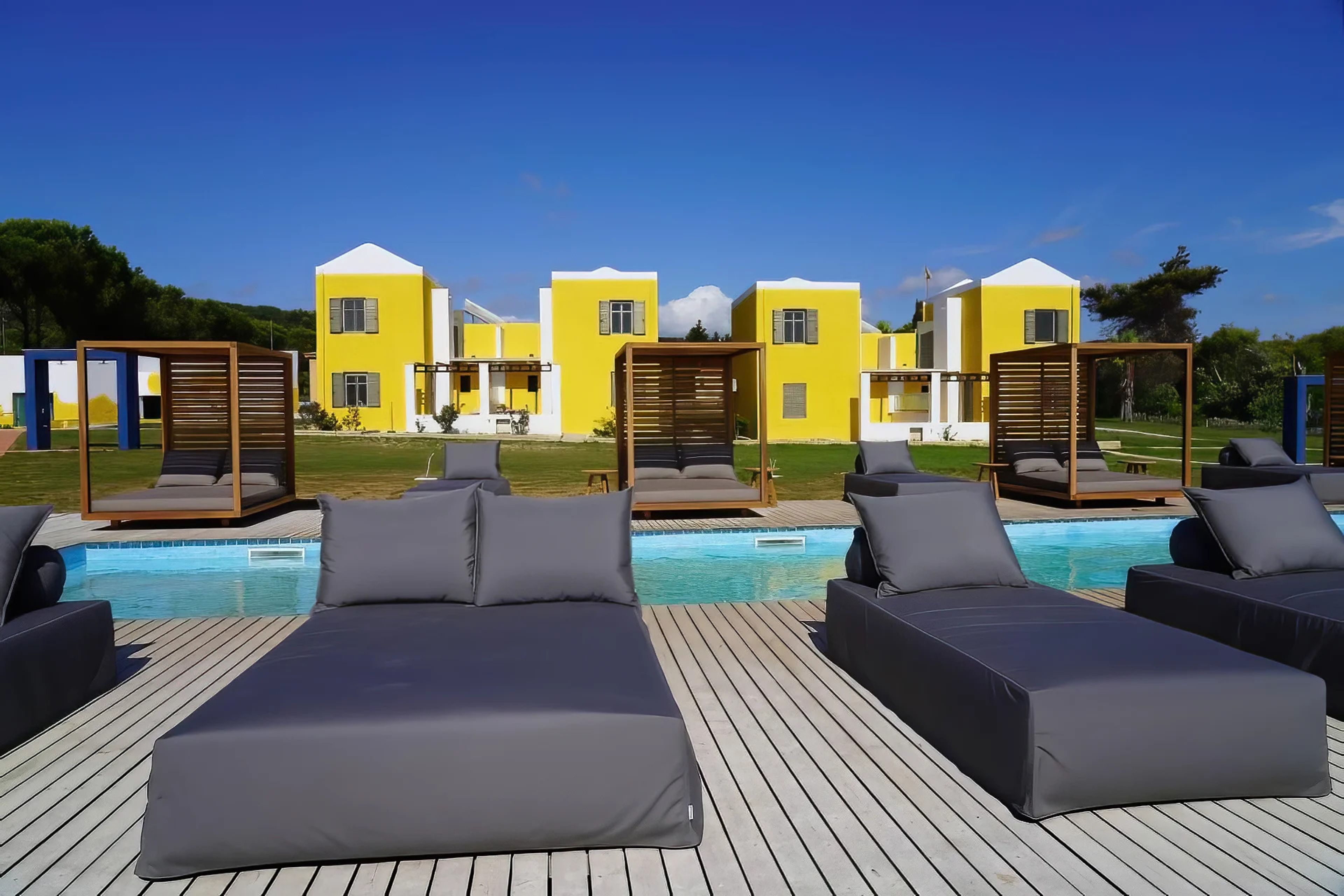 A poolside area with lounge chairs and a pool, surrounded by yellow buildings with white accents.