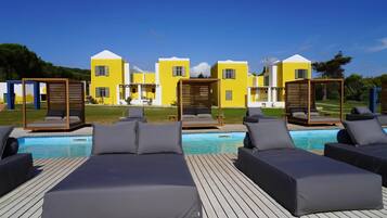 A poolside area with lounge chairs and a pool, surrounded by yellow buildings with white accents.