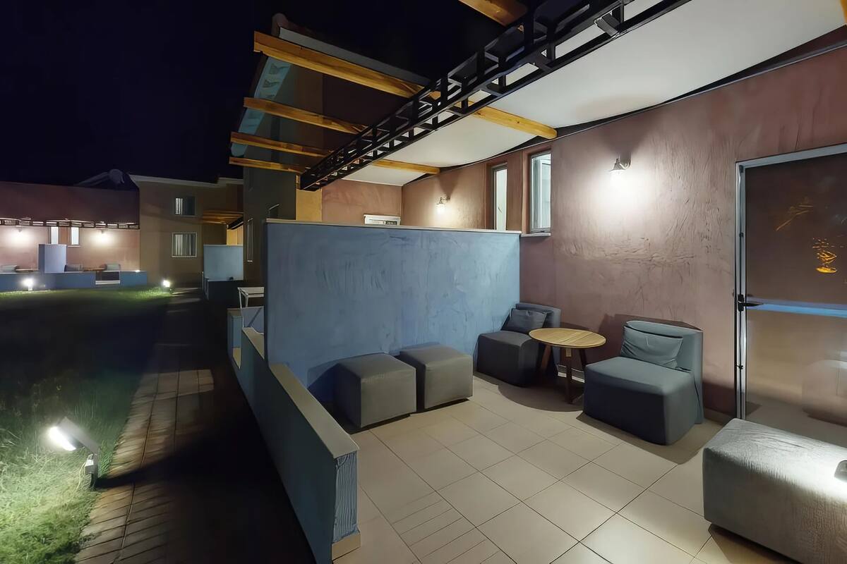 A modern outdoor seating area with cushioned sofas and a small round table, a staircase, and a view of the surrounding buildings.