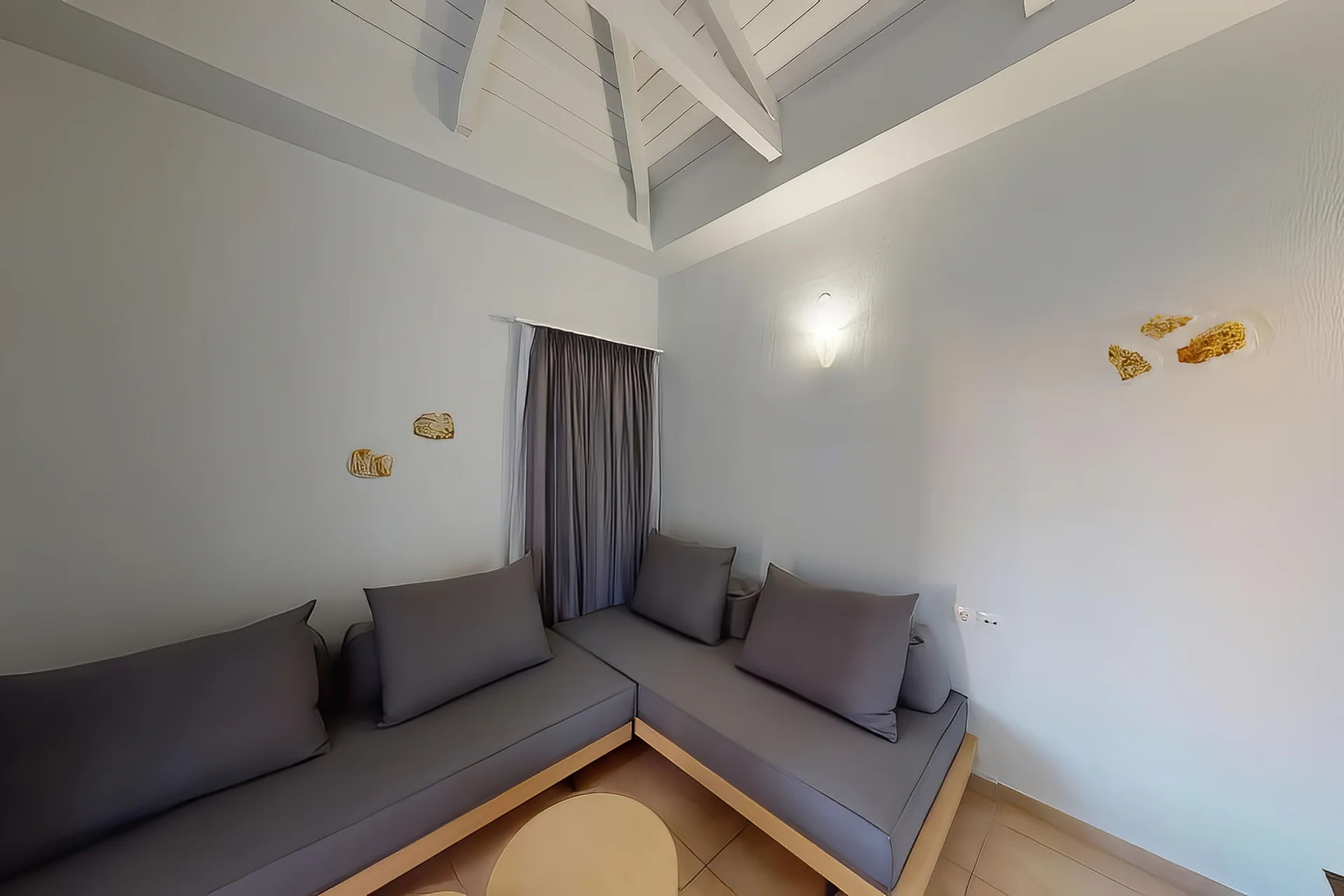 Un soggiorno moderno con un divano componibile, una finestra con tende, un soffitto con travi a vista e un lampadario a parete.