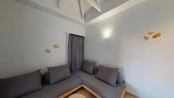 A modern living room with a sectional sofa, a window with curtains, a ceiling with exposed beams, and a wall-mounted light fixture.