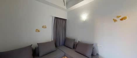 Una sala moderna con un sofá modular, una ventana con cortinas, un techo con vigas a la vista y un aplique de pared.