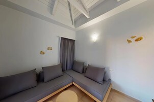 Una sala moderna con un sofá modular, una ventana con cortinas, un techo con vigas a la vista y un aplique de pared.