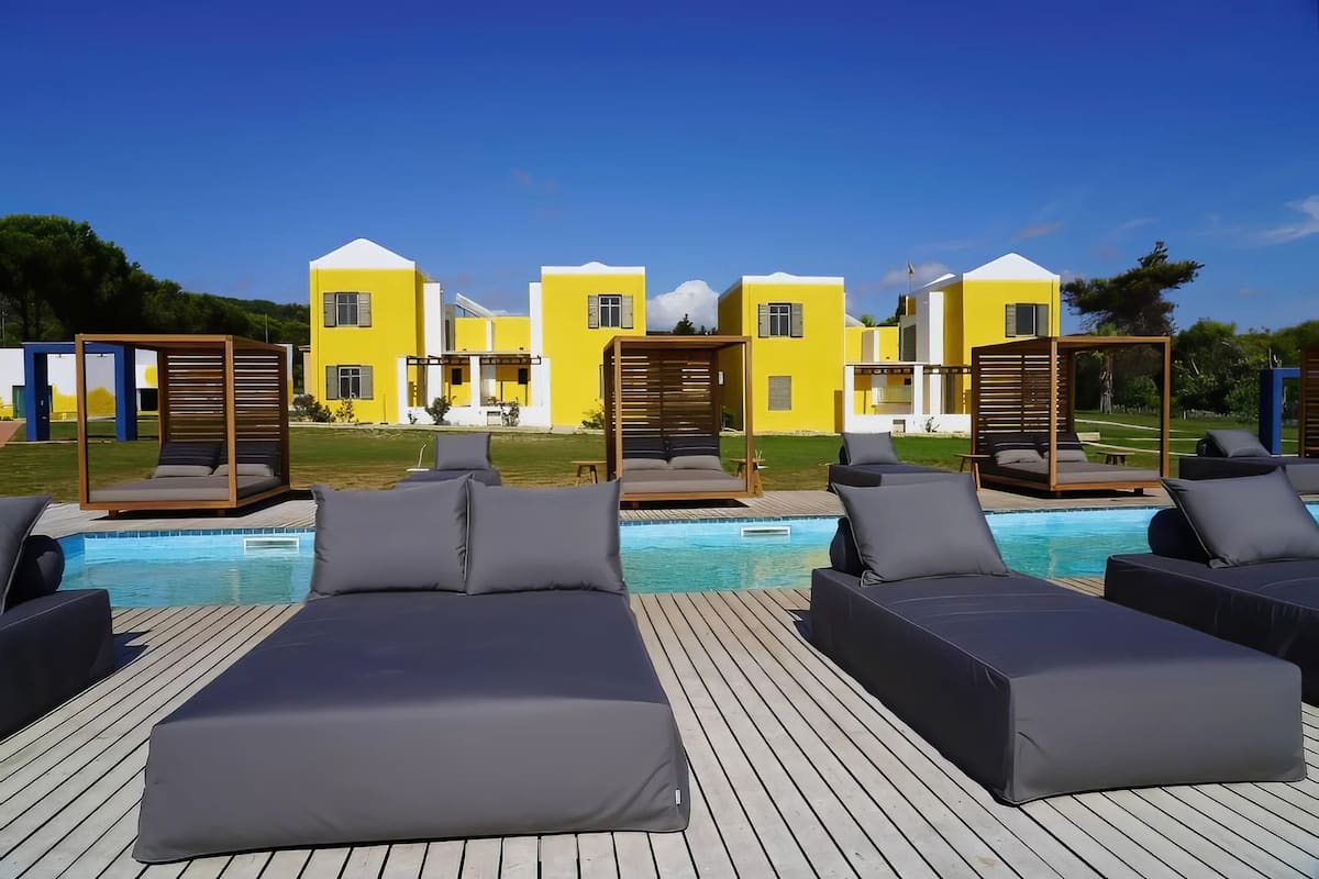A poolside area with lounge chairs and a pool, surrounded by yellow buildings with white accents.