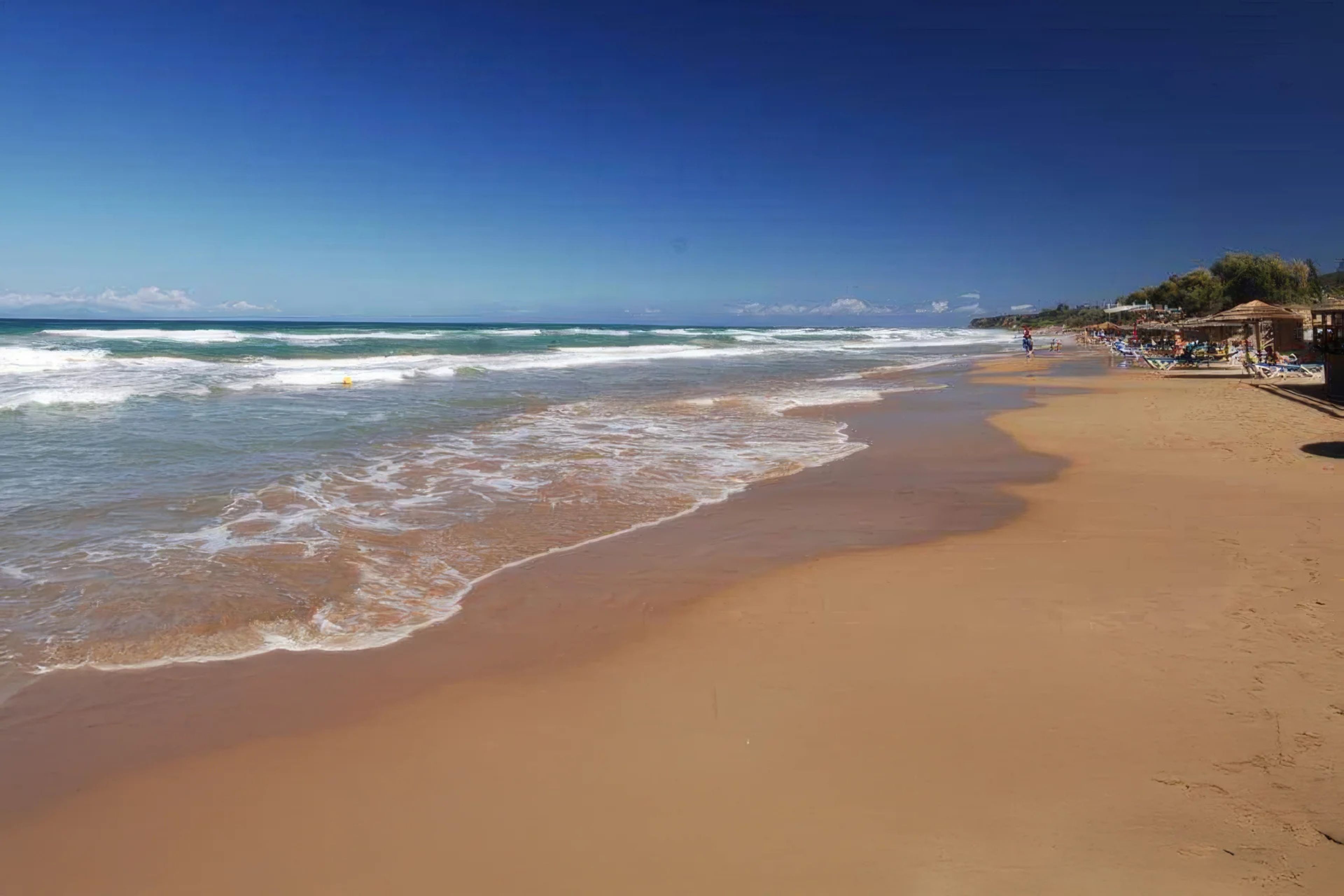 Une plage avec un ciel dégagé, des vagues et quelques personnes.