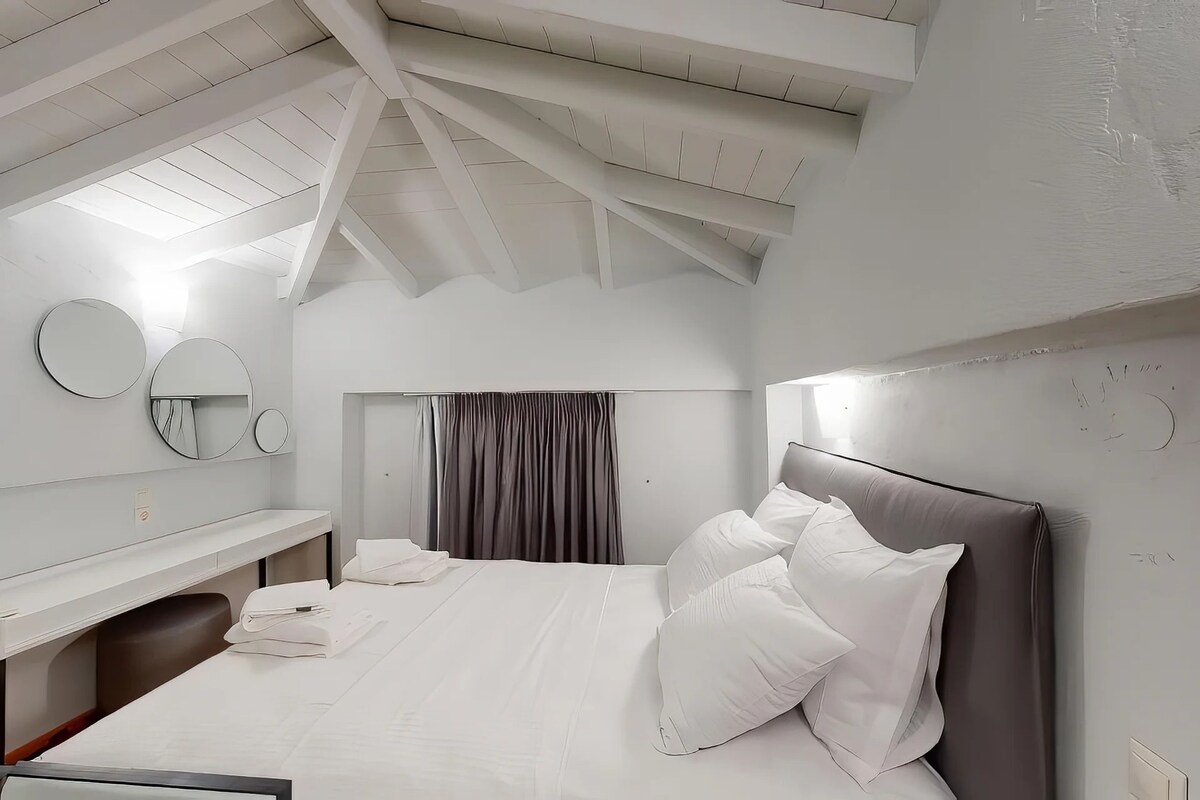 A modern hotel room with a large bed, a desk, and a mirror.
