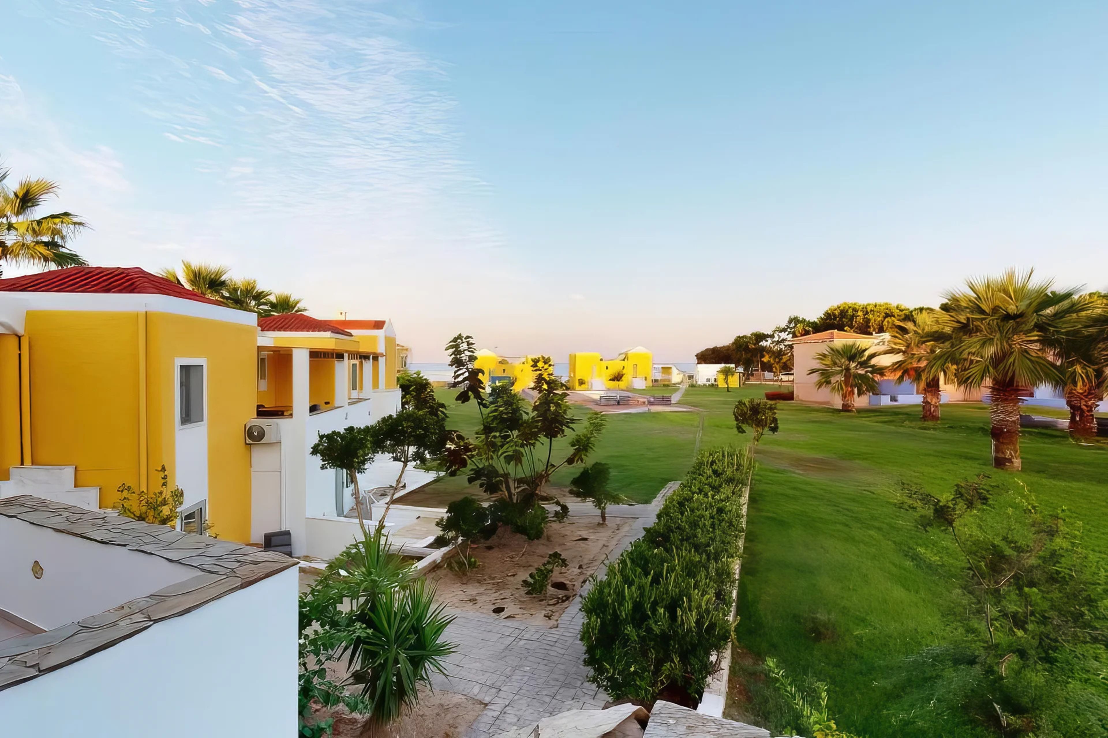 Una zona residencial con edificios de color amarillo y blanco, un césped cuidado y palmeras.
