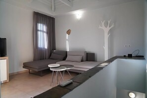 Una sala de estar moderna con un sofá, dos mesitas auxiliares, un televisor de pantalla plana y un adorno en la pared.