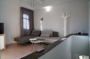 Una sala de estar moderna con un sofá, dos mesitas auxiliares, un televisor de pantalla plana y un adorno en la pared.