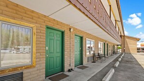 A row of green doors with a brick facade, a covered walkway, and outdoor seating. - The Alpine Motel (Collbran)