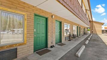 A row of green doors with a brick facade, a covered walkway, and outdoor seating.