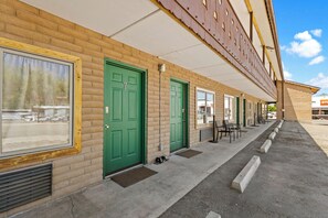 A row of green doors with a brick facade, a covered walkway, and outdoor seating. - The Alpine Motel (Collbran)
