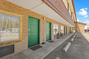 A row of green doors with a brick facade, a covered walkway, and outdoor seating.