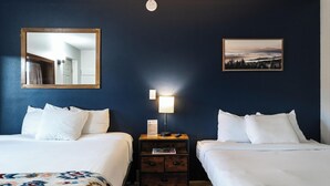 A hotel room with two beds, a nightstand with a lamp, a mirror, and a framed picture on the wall. - The Alpine Motel (Collbran)