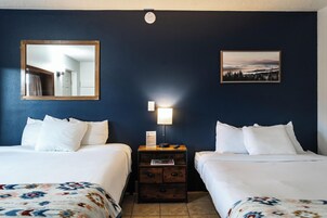 A hotel room with two beds, a nightstand with a lamp, a mirror, and a framed picture on the wall.