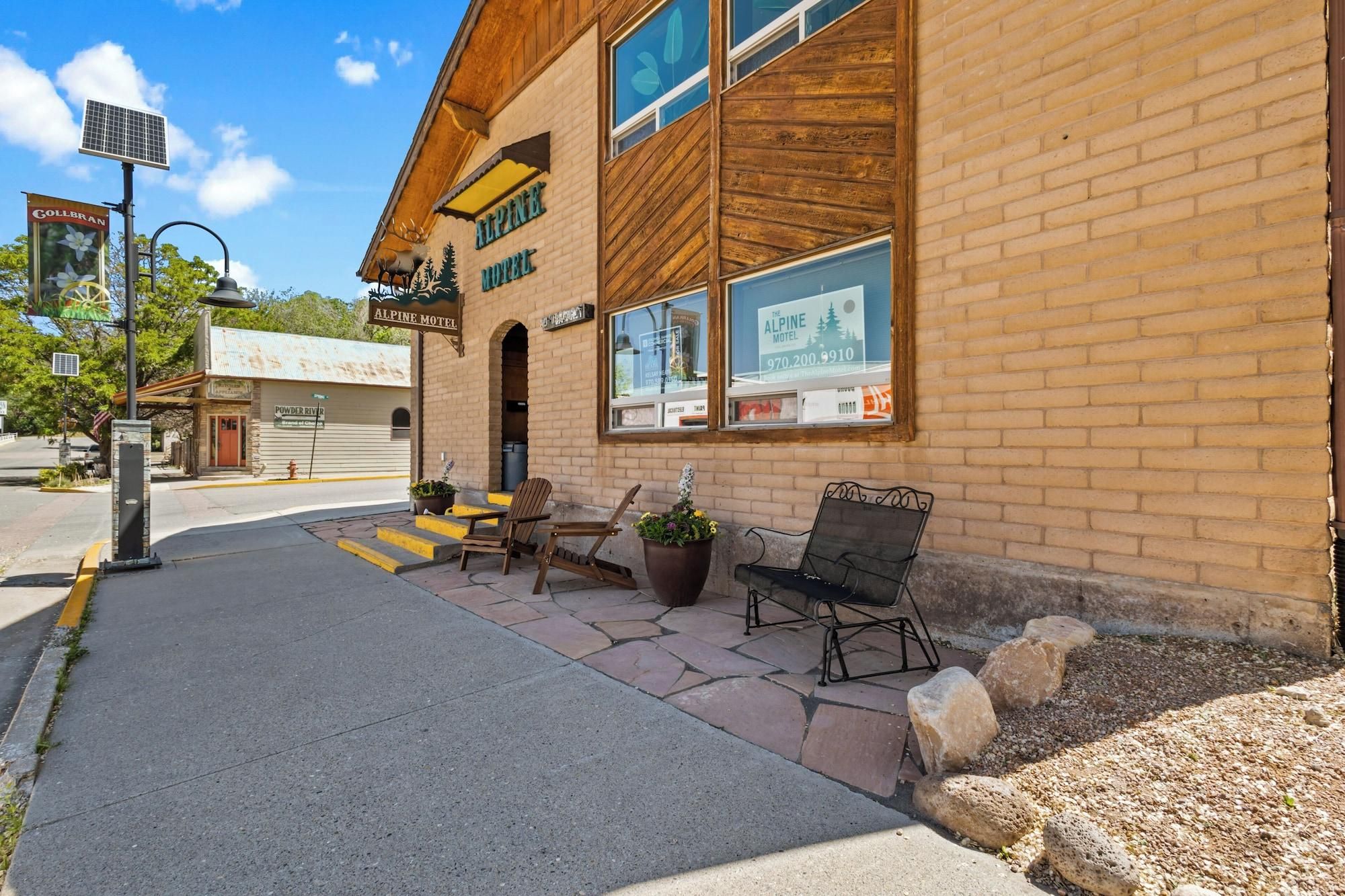 A brick building with a sign for the Alpine Motel, outdoor seating, and a solar panel.