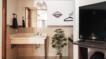 Un baño con lavamanos, espejo, toallero, planta en maceta y televisión.