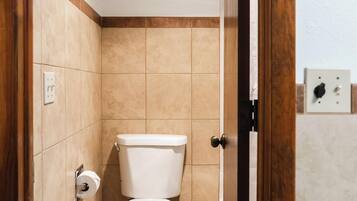Un baño pequeño y cerrado con inodoro, ducha y puerta de madera.