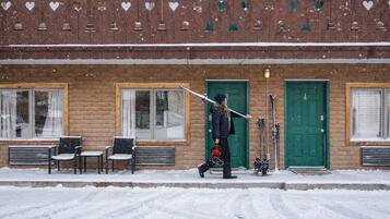 A building with a brick facade, multiple windows, and doors. There are benches outside and a person carrying skis.