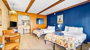 A hotel room with two beds, a wooden ceiling, a blue wall, a TV, a desk, and a chair. - The Alpine Motel (Collbran)