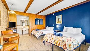 A hotel room with two beds, a wooden ceiling, a blue wall, a TV, a desk, and a chair.