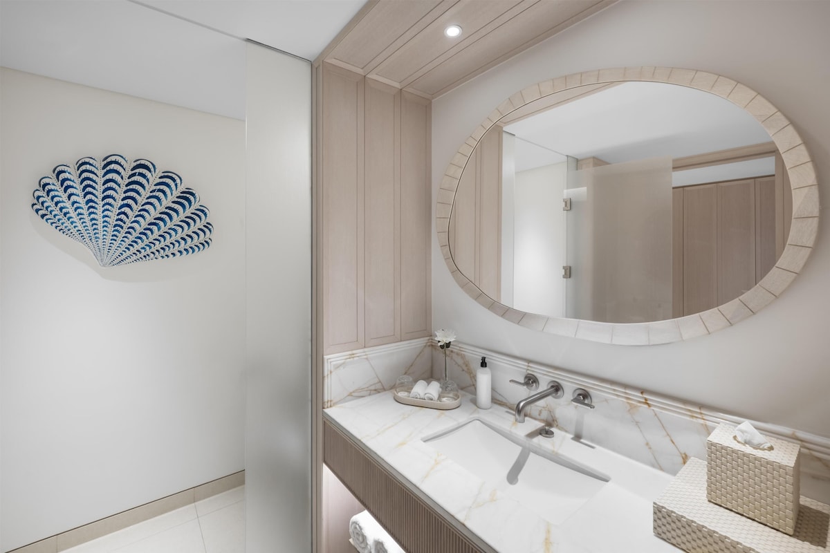 A modern bathroom with a marble sink, a large mirror, and a decorative shell wall art piece.