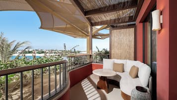 A balcony with a white sofa, a round table, and a view of a beach and pool.