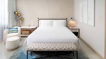 Una habitación de hotel con cama, mesitas de noche, un escritorio, una silla y un banco.