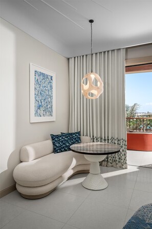 Un salon moderne avec un canapé, une table ronde, un luminaire suspendu et une grande fenêtre avec des rideaux.