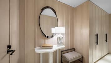 Una habitación con paneles de madera, una consola blanca con un libro y una lámpara, un pequeño banco, un espejo y una puerta con pomo.