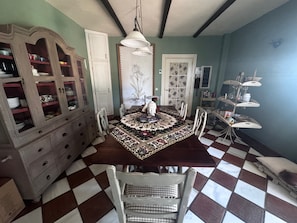 Ein Esszimmer mit Schachbrettmuster-Boden, einem großen, hölzernen Schrank mit Glastüren und einer gemusterten Tischdecke.