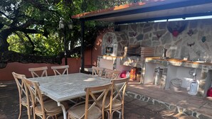 An outdoor patio with a stone wall, a brick barbecue, and a table with chairs. - Luxury Villa with All Amenities in Marbella – Pool, Jacuzzi, Barbecue, Wood-Fired Oven (Benahavís)