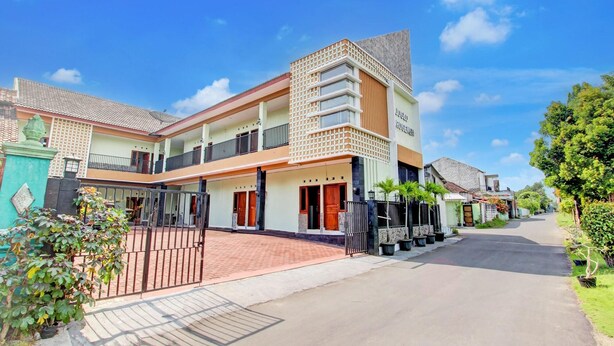 A two-story residential building with a gated entrance, a balcony, and a driveway leading to the street. - Oyo 94249 Joglo Sorogenen (Kalasan)