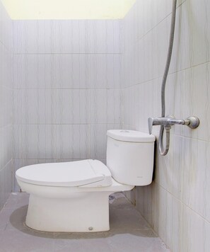 A bathroom with a toilet, a shower, and a tiled wall. - Oyo 94249 Joglo Sorogenen (Kalasan)