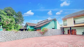 A courtyard with a paved walkway, stone wall, and two buildings with tiled roofs. - Oyo 94249 Joglo Sorogenen (Kalasan)