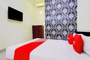 Une chambre avec un lit, un téléviseur fixé au mur, une armoire et un rideau à motifs.