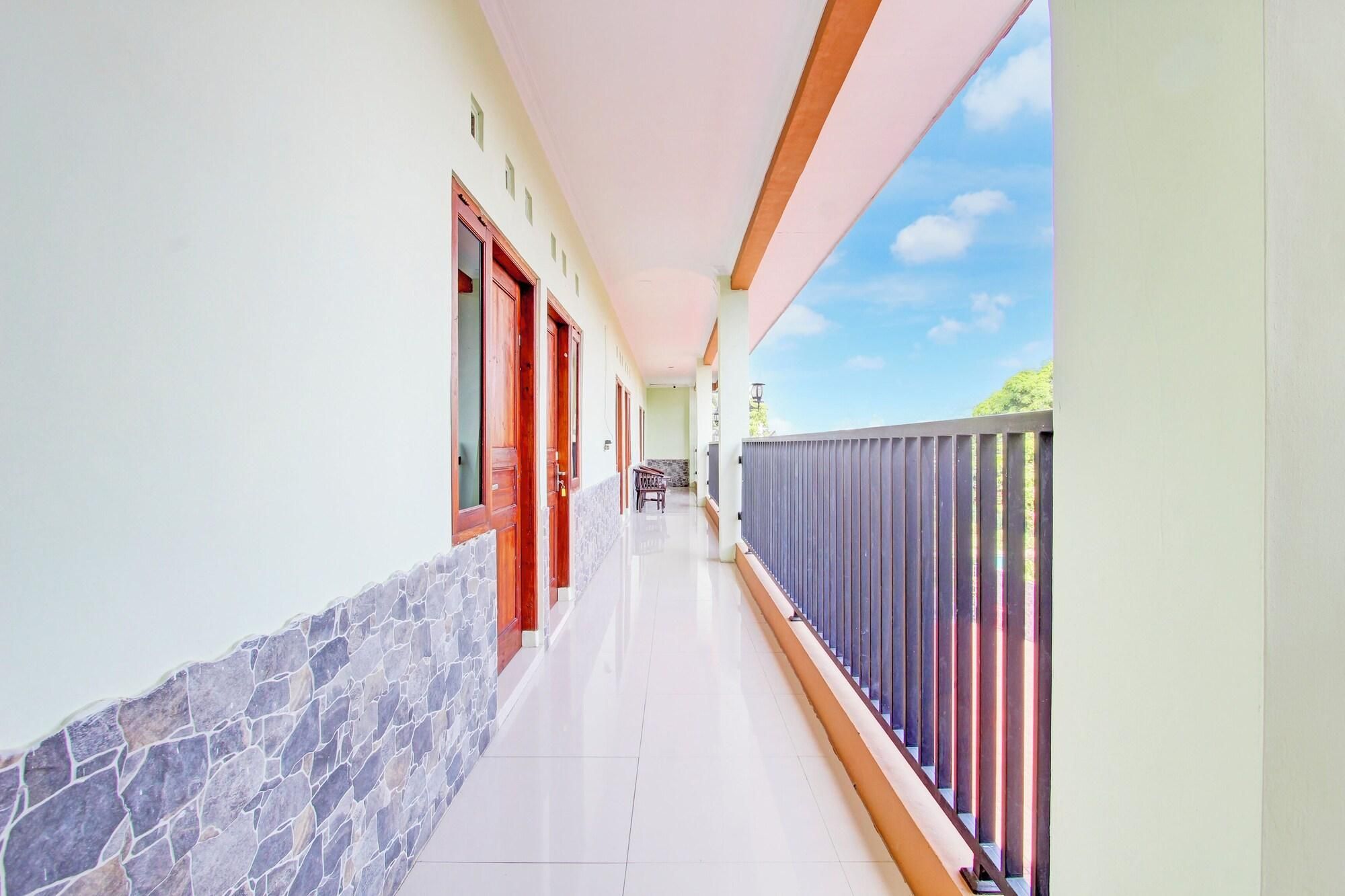 A corridor with a stone wall, wooden doors, and a balcony with a metal railing.