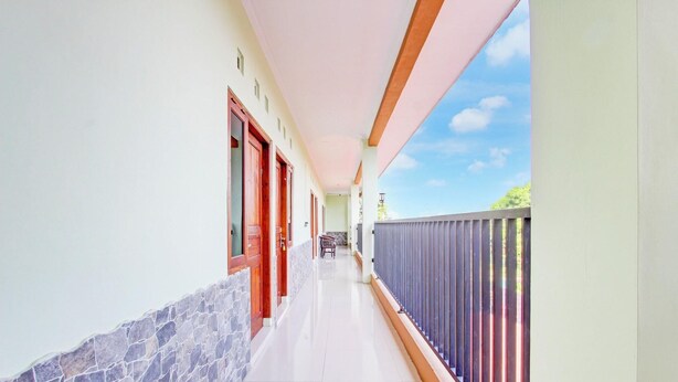 Ein Korridor mit einer Steinwand, Holztüren und einem Balkon mit Metallgeländer.