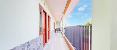 A corridor with a stone wall, wooden doors, and a balcony with a metal railing.