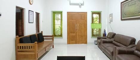 Un salon comprenant un canapé en bois, un canapé en cuir marron, un banc en bois, une porte avec un vitrage vert et un climatiseur fixé au mur.