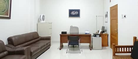 A room with a brown leather sofa, a desk with a chair, a white cabinet, and a wooden door.
