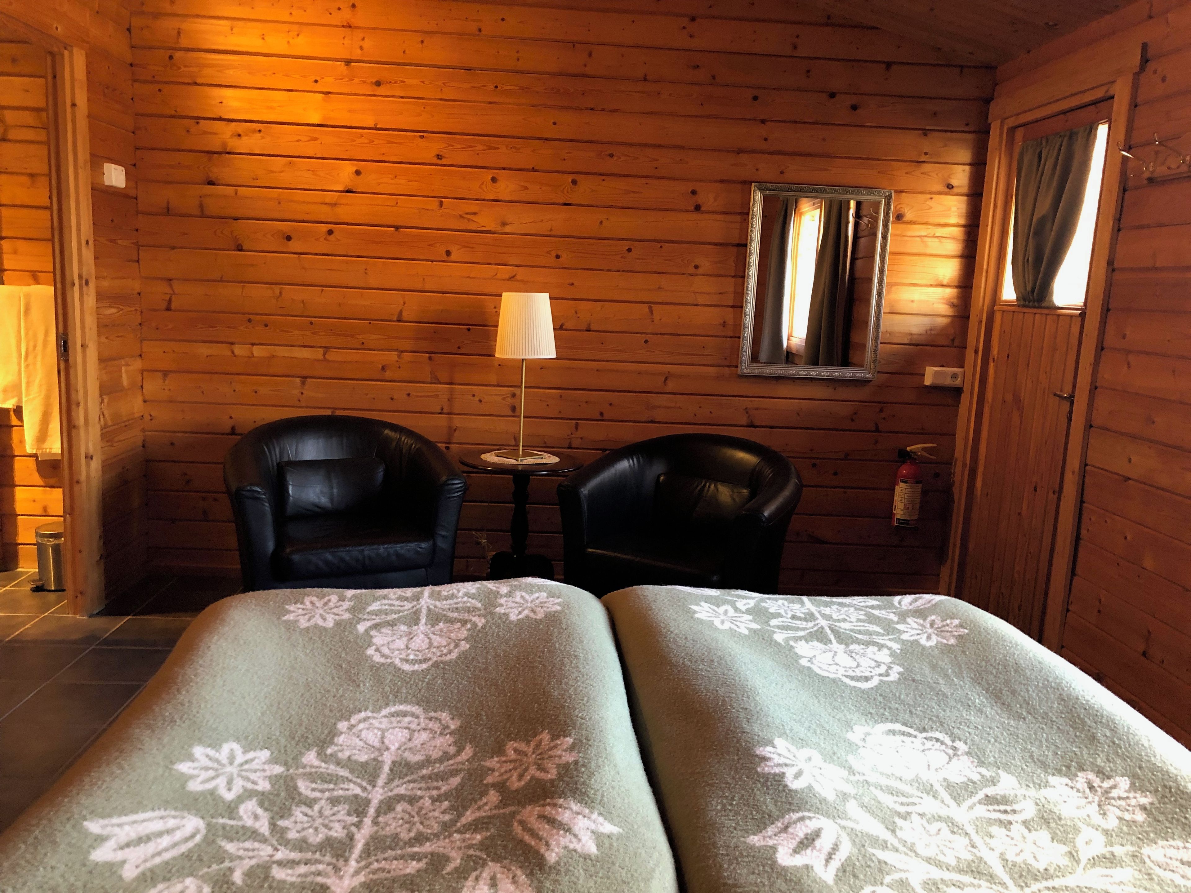 A wooden cabin room with two leather chairs, a small table, a lamp, and a mirror on the wall.