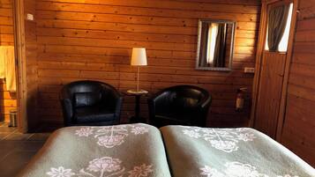 A wooden cabin room with two leather chairs, a small table, a lamp, and a mirror on the wall.