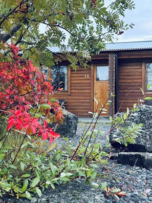 A wooden cabin with a number '14' on the door, surrounded by autumn foliage and rocks. - Vogafjós Farm Resort (Myvatn)