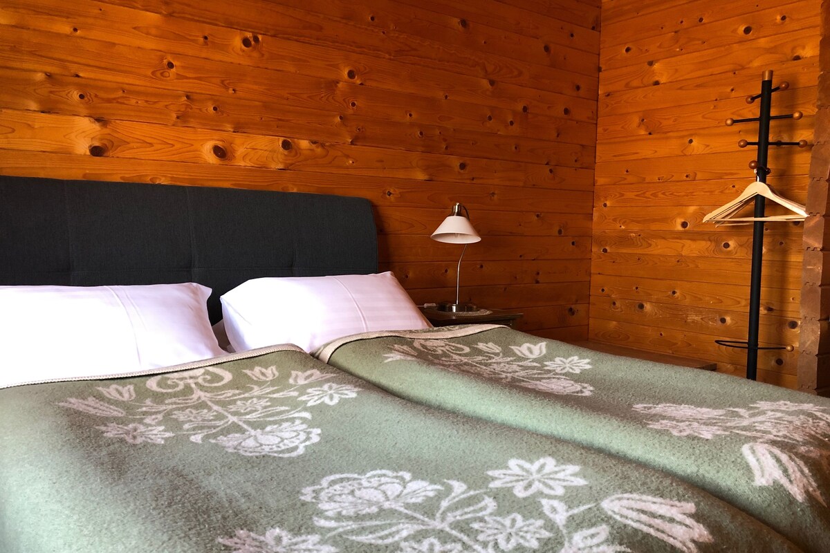 Una habitación de cabaña de madera con cama, almohadas, lámpara y perchero.