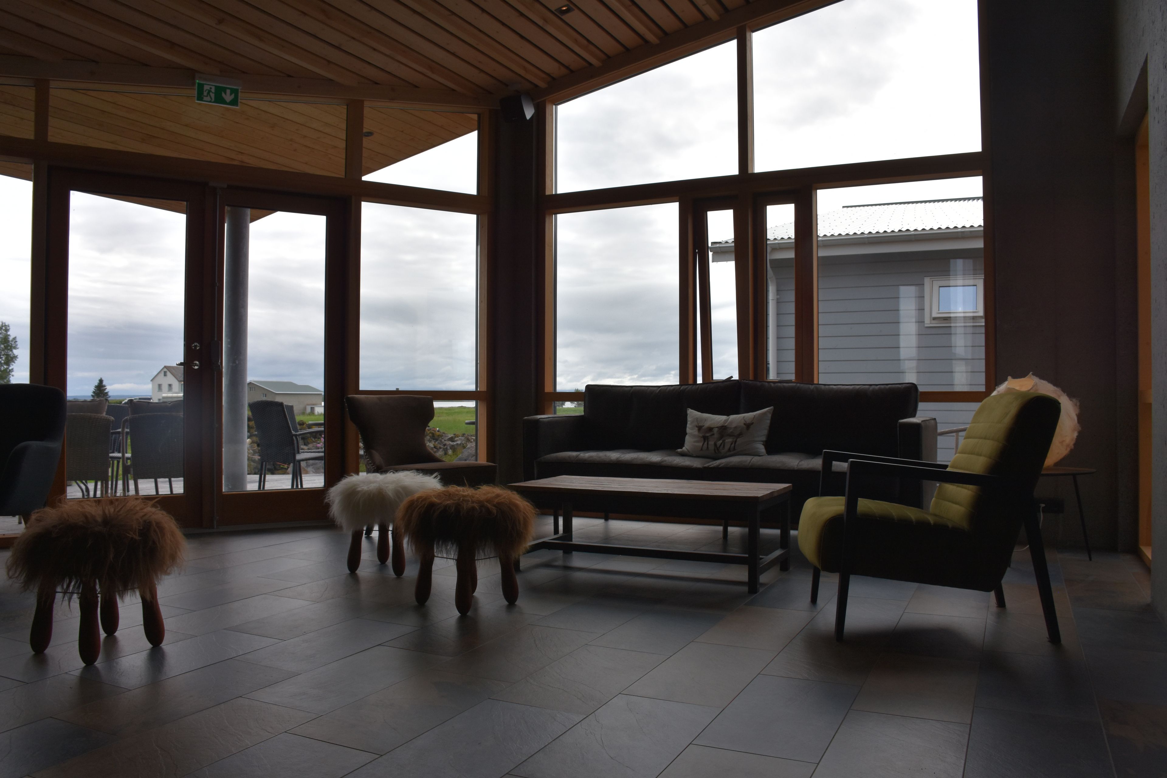 A spacious room with large windows, a sofa, a coffee table, and two fluffy stools.
