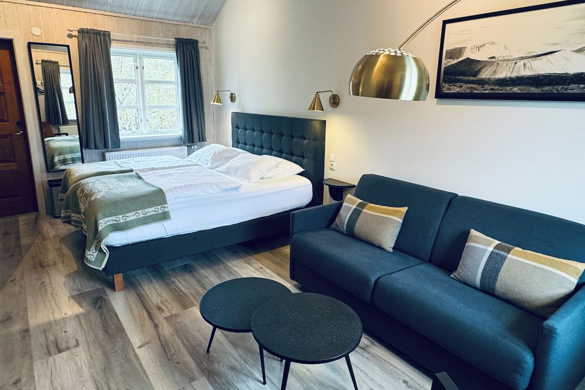 Et soveværelse med en dobbeltseng, en blå sofa, et lille bord, en lampe og et billede i ramme på væggen.